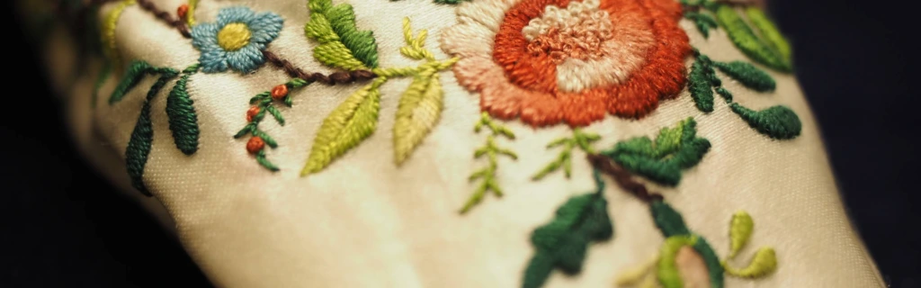 Kirjo-ommeltu kukka häätossujen päällä. Broderad blomranka på en brudtoffla. Embroidered flowers on a bridal slipper.